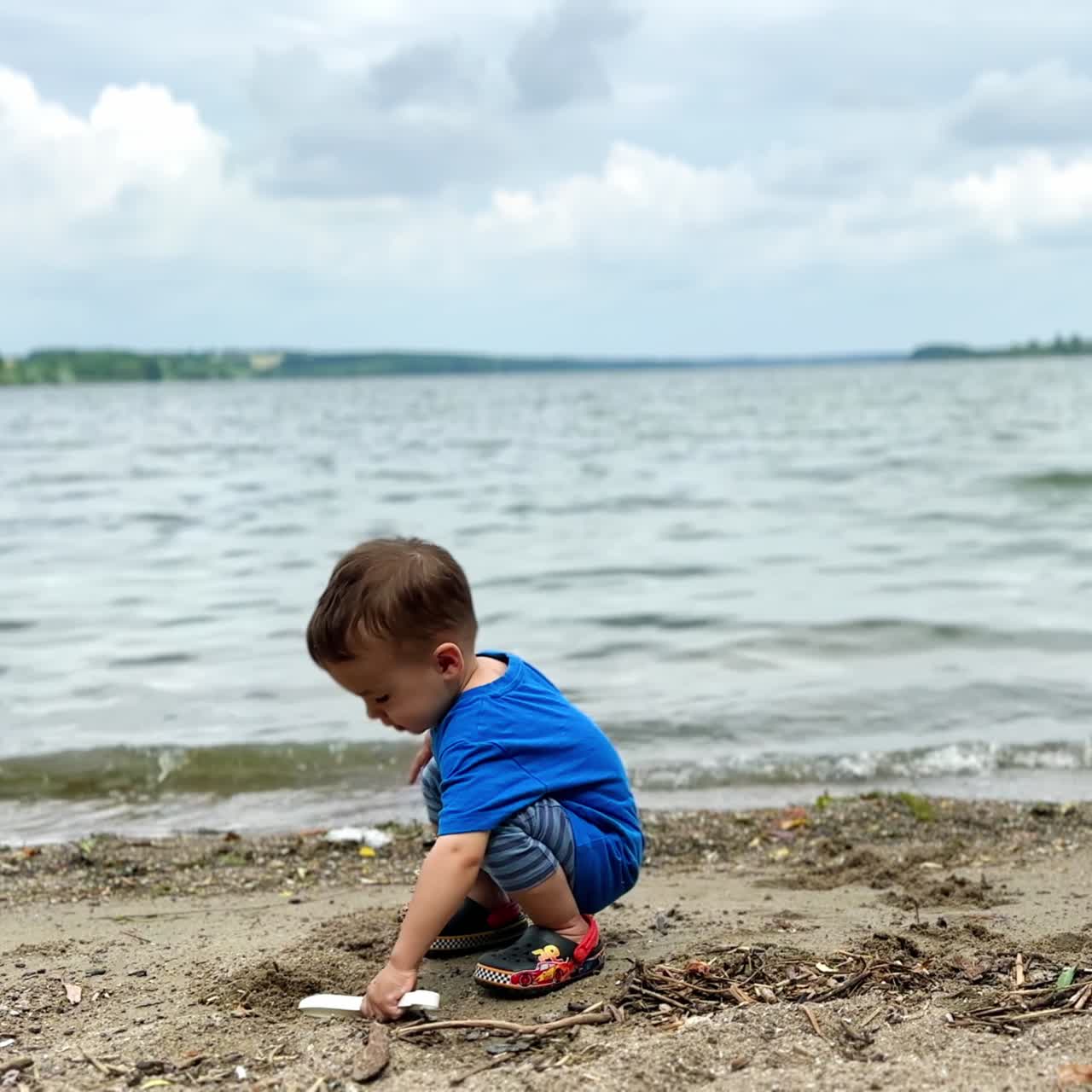 Caucasian child sitting on the beach digging sand with his shovel. Cheerful baby throws the sand at the beach