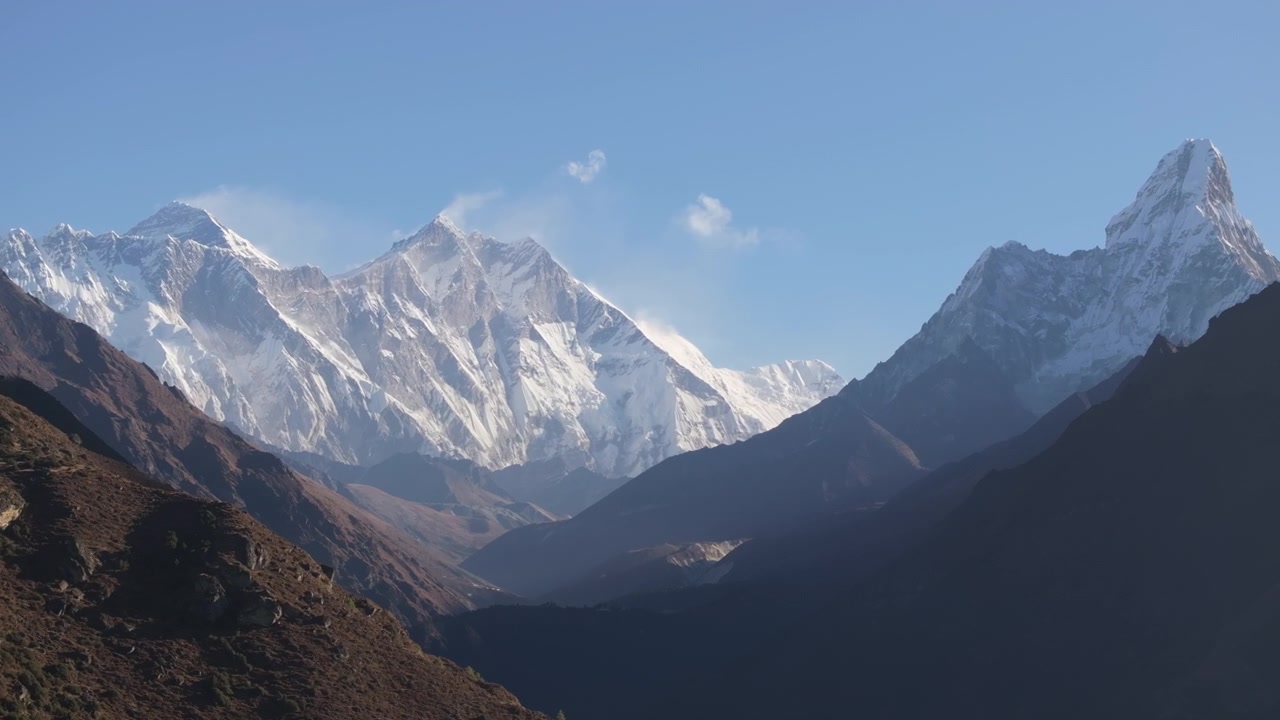 Regione dell'Everest, Nepal. Ripresa laterale con drone che si muove oltre un pendio roccioso per rivelare una vista mozzafiato dell'Ama Dablam, del Monte Everest e del Lhotse sotto un cielo azzurro e limpido