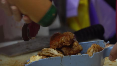 puesto de comida callejera preparando pedidos para llevar, condimentando con deliciosa pimienta blanca, cinco especias, ajo y chile en polvo sobre pollo frito recubierto de miel de soja en el famoso mercado nocturno de taiwán, asia