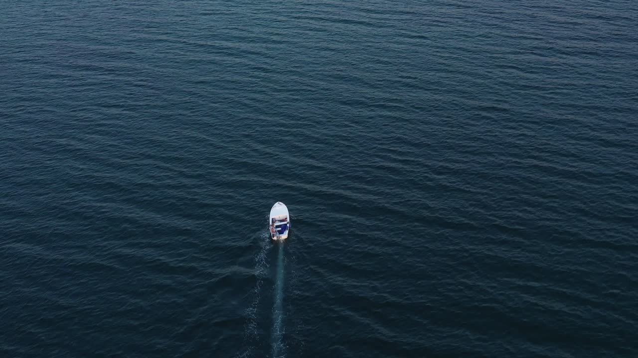 Un drone aereo segue una piccola barca bianca su una distesa di acque aperte