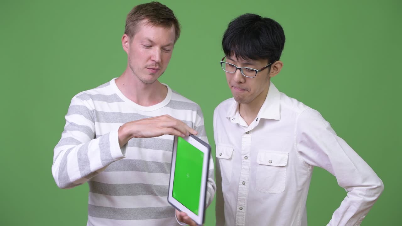 두 명의 행복한 젊은 다민족 사업가들이 디지털 태블릿을 보여주고 엄지손가락을 올리고 있습니다.