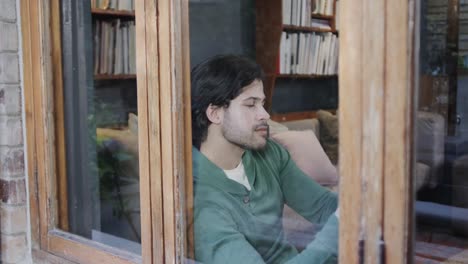 hombre caucásico feliz usando un teléfono inteligente sentado junto a la ventana en casa, cámara lenta