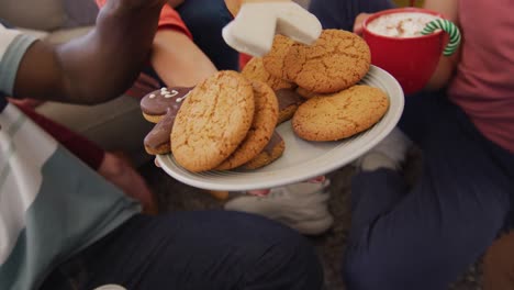 Midsection-of-group-of-diverse-friends-eating-christmas-cookies