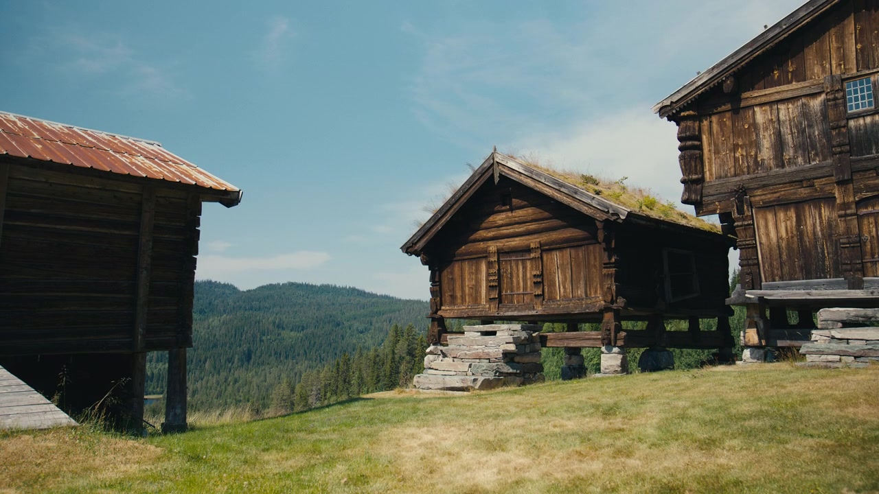 Historiske norske trælagerbygninger med græstage, der har udsigt over skovklædte bakker, og som fremviser traditionel nordisk arkitektur, landlig kulturarv og naturskønne landskaber.