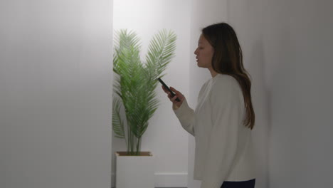 stressed or anxious woman leaning against wall at home reacting to internet or social media news message or story on mobile phone 1