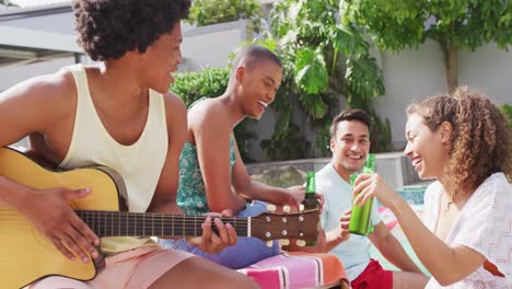 hombre afroamericano tocando la guitarra mientras varios amigos hacen brindis con cerveza en la fiesta de la piscina