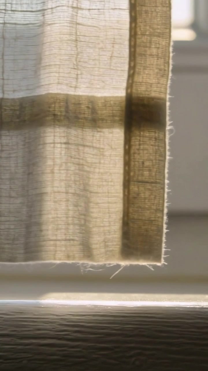 Video verticale: Tenda trasparente che si solleva per la brezza a casa, mostrando il telaio della finestra e una striscia di sole sul davanzale