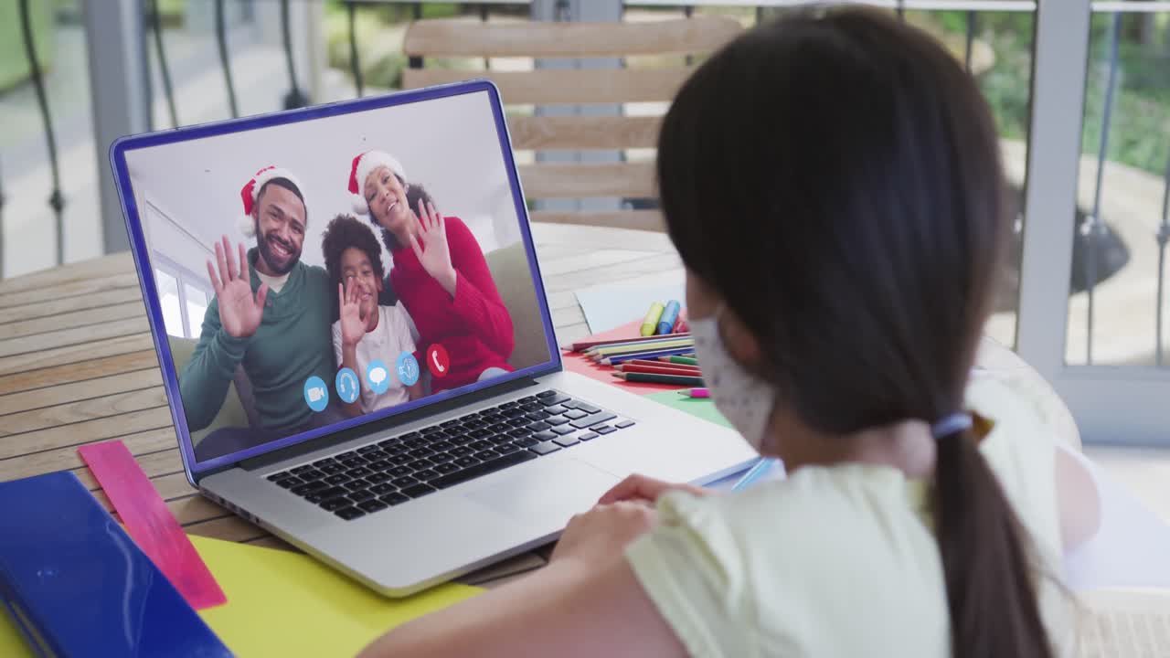 chica caucásica con máscara facial, usando computadora portátil en video chat con la familia saludando durante la navidad en