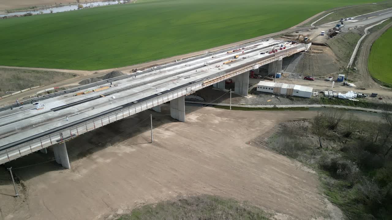 Bridge under construction in a rural area, showing progress, surrounding fields, and equipment