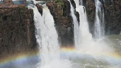 slow motion tracking view of beautiful colourful group of waterfalls eroding rock, falling into beautiful rainbow pool, bright rainbow in front of amazing rocky waterfall landscape in iguazu falls