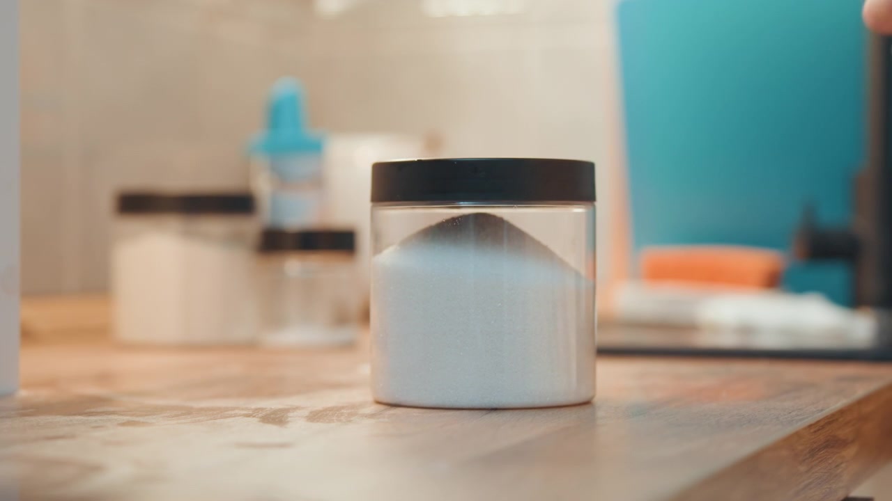 Close up hands sealing sugar jar, placing lid on glass container on wooden counter, routine pantry storage for baking, careful motion with small bracelet visible, tidy home kitchen finish