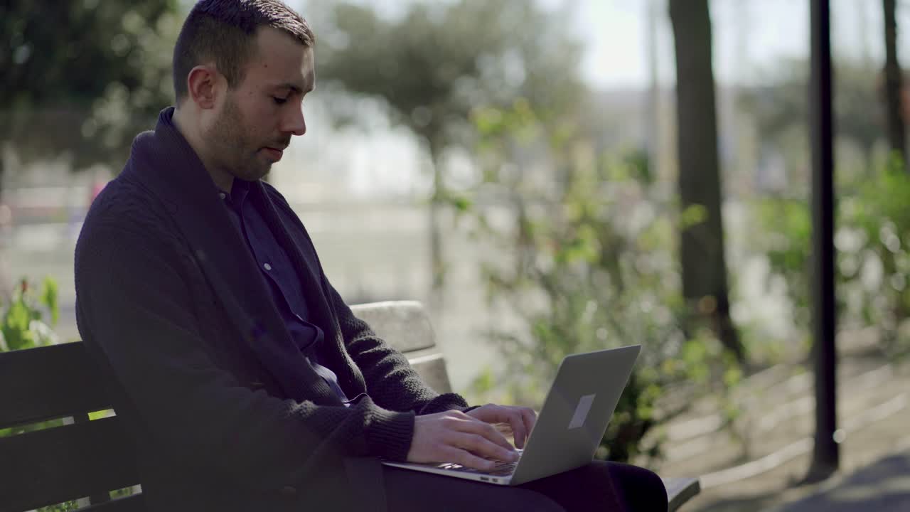 Focused handsome young man typing on laptop outdoor