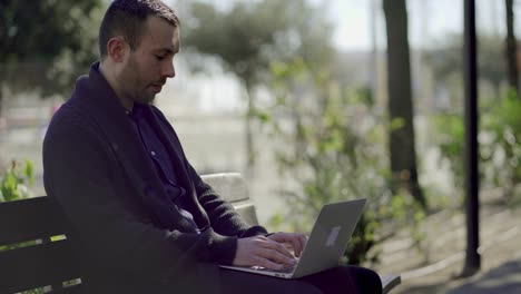 joven guapo enfocado escribiendo en una computadora portátil al aire libre