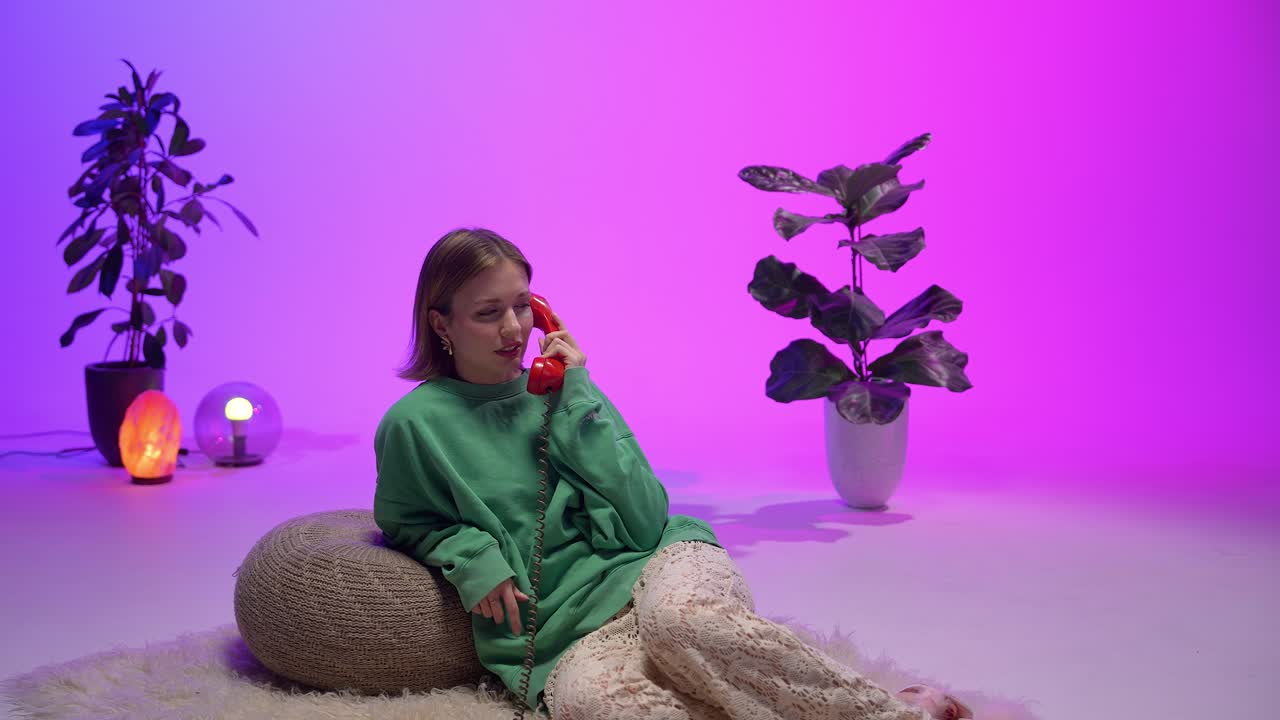Fashionable woman lounging on fluffy rug speaks on a red rotary phone in a colorful retro-inspired room with ambient lights, potted plants, and cozy textures that evoke nostalgia and comfort