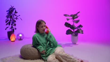 fashionable woman lounging on fluffy rug speaks on a red rotary phone in a colorful retro-inspired room with ambient lights, potted plants, and cozy textures that evoke nostalgia and comfort