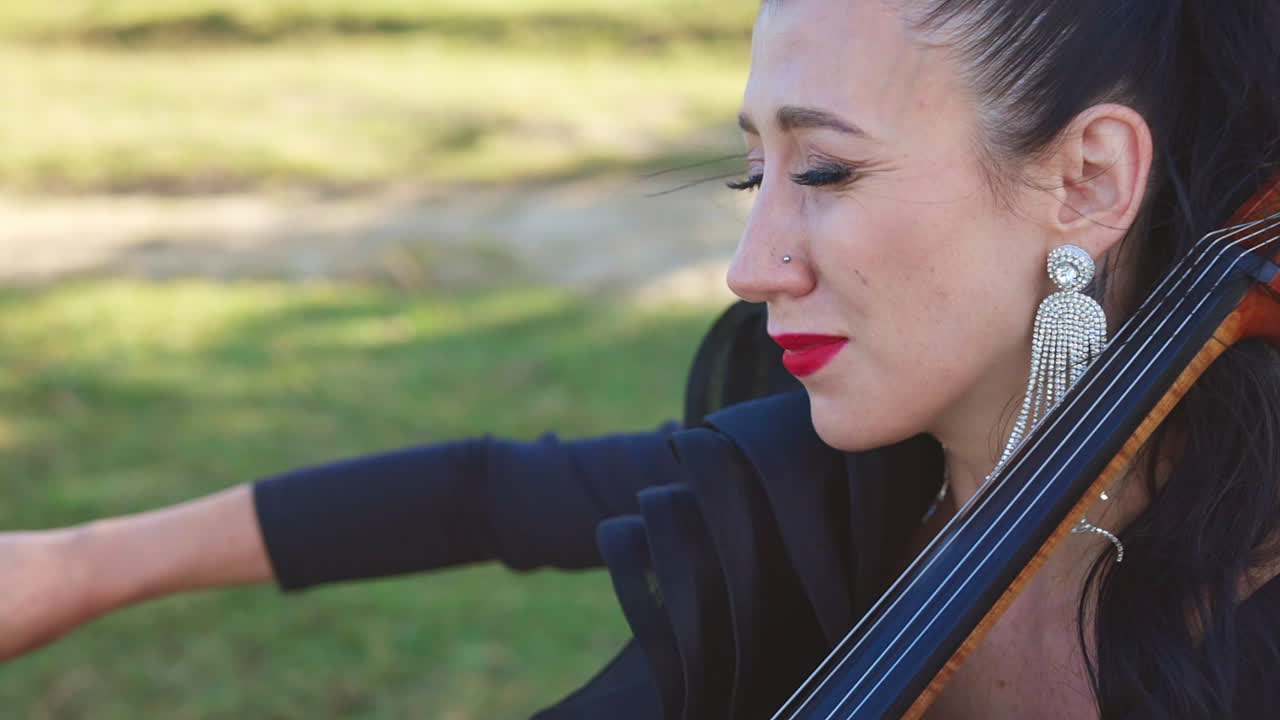 Woman with bright makeup plays classical music emotionally. Close-up. Playing cello in the nature backdrop.