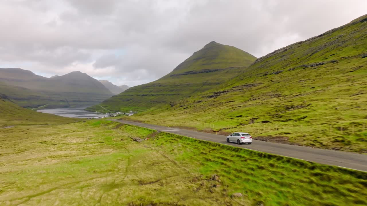 A car drives on a scenic road with green mountains in the Faroe Islands