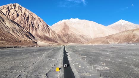 aerial drone shot showcasing a car on an endless road in ladakh, vanishing into the mountain horizon.