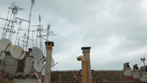 the tiled roof of the house and a large number of television antennas and satellites on it, against a cloudy sky