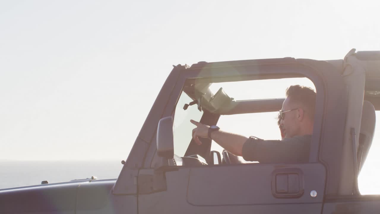 Happy caucasian gay male couple in car admiring the view and pointing on sunny day at the beach