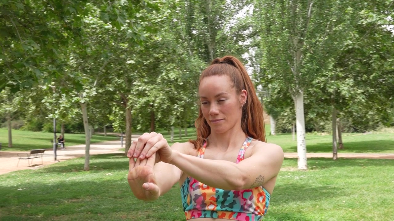 Una mujer realiza estiramientos de brazos en un animado parque para promover el fitness y el bienestar.