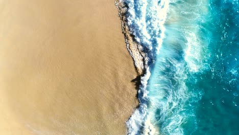 aerial view waves break on white sand beach.