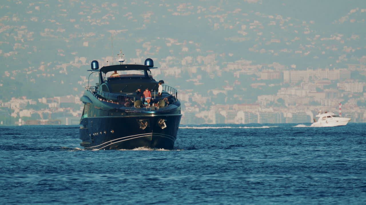 Cannes, France - October 16, 2025: Elegant black yacht sailing across calm sea with a scenic coastal city backdrop