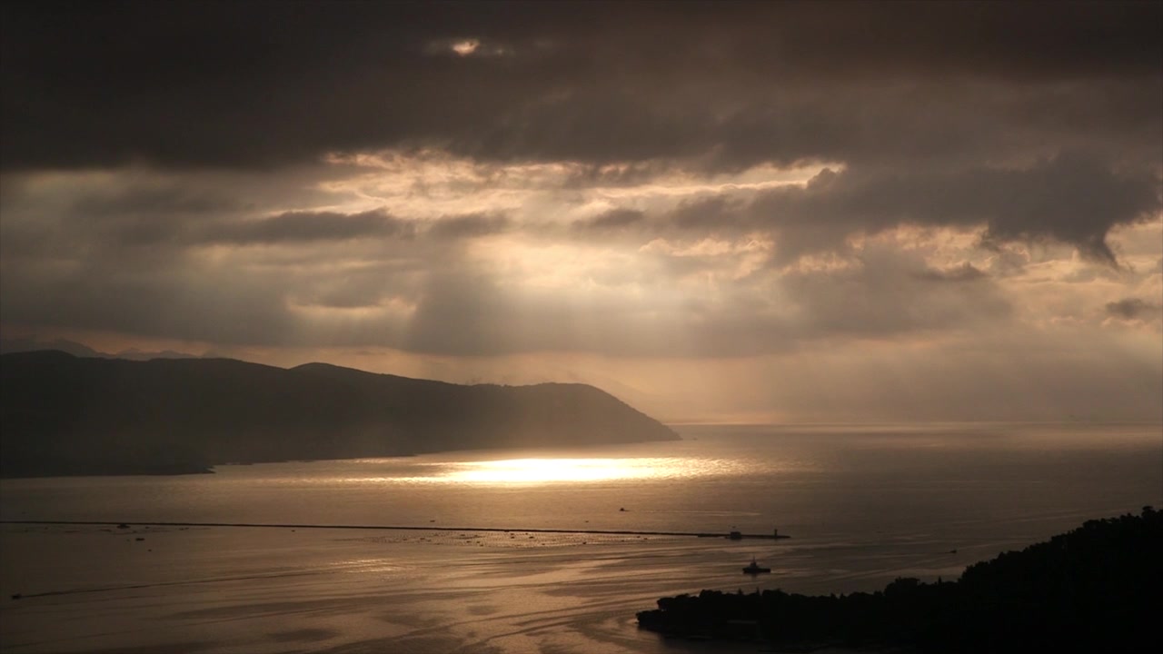 Sunset over the Gulf of La Spezia, Italy, with golden light reflecting across the sea, silhouetted coastal hills, boats, and dramatic clouds.