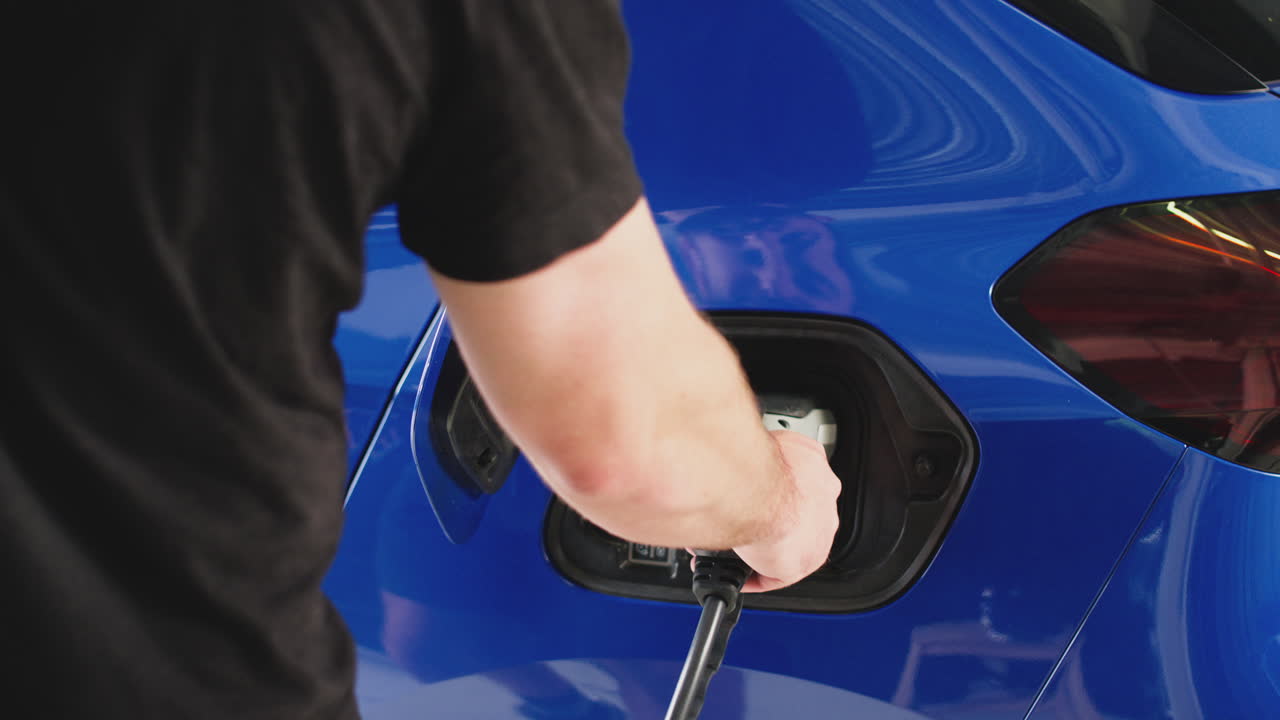 배터리 수준을 모니터링하기 위해 휴대폰 앱을 사용하여 케이블로 전기 자동차를 충전하는 사람