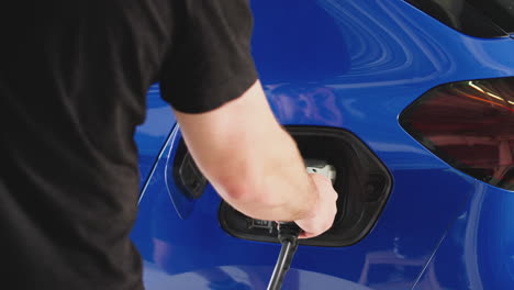 hombre cargando un coche eléctrico con cable usando una aplicación en el teléfono para monitorear el nivel de la batería