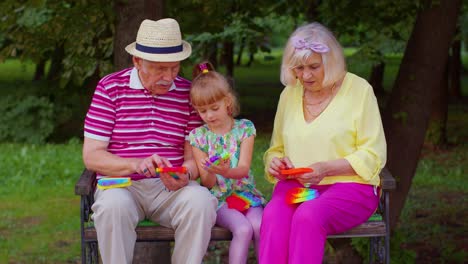una pareja elegante, abuela, abuelo y nieta juegan al juego antiestrés pop it.