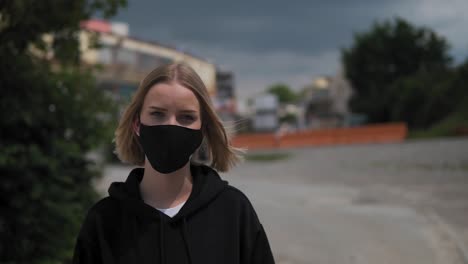 portrait of young woman with black face mask looking at camera in urban exterior slow motion, covid-19 virus pandemic outbreak concept