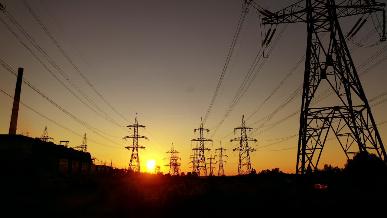 Electric towers against the orange sunset. High voltage electric lines in the evening. Silhouettes of electrical pylons.