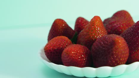 fresh big red tasty ripe strawberries rotates slowly on a white plate on light blue background, healthy food concept, medium close up shot, camera rotate left