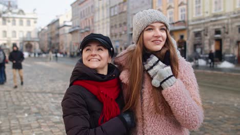 two women smile and walk through the city together in winter