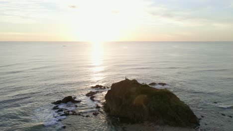 drone de 4k se acerca lentamente y luego vuela sobre una roca gigante de la playa durante la majestuosa puesta de sol