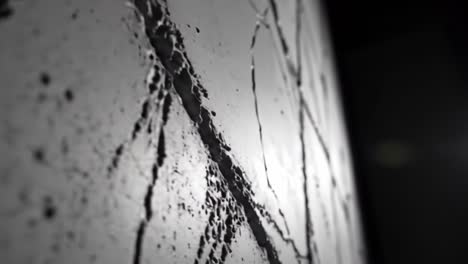 abstract close-up of a textured surface with water droplets and cracks, highlighting the interaction between light and reflection in a minimalistic setting