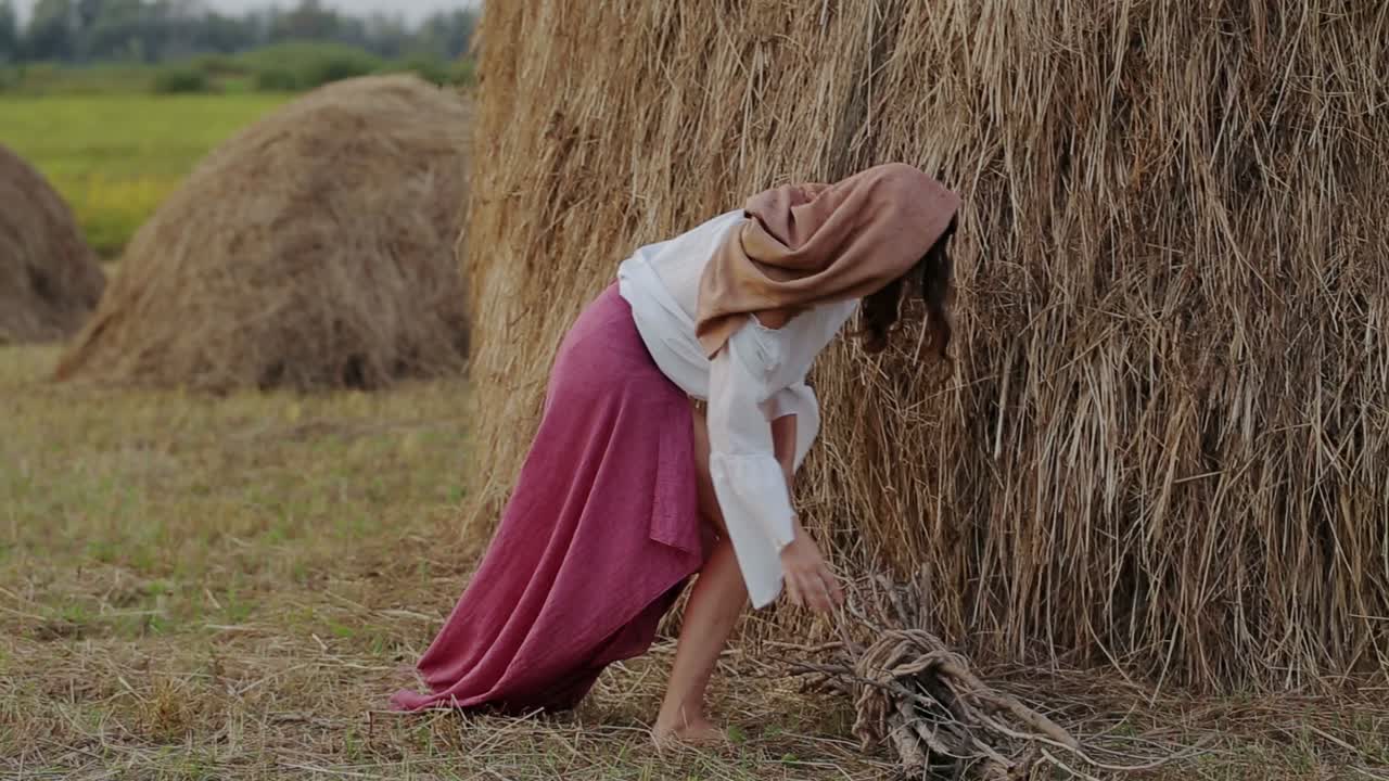Woman gathering firewood near haystacks