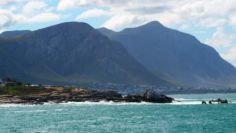 Waves-crash-on-Hermanus-coastline-with-Klein-River-mountains-in-back,-telephoto