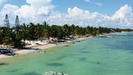 Drohne-Aus-Der-Luft,-Die-An-Einem-Sommertag-Rechts-Von-Der-Küste-Eines-Kleinen-Fischerdorfes-Im-Naturschutzgebiet-Sian-Ka&#39;an-In-Der-Nähe-Von-Tulum,-Mexiko,-Mit-Kleinen-Fischerbooten,-Pfeilern,-Palmen-Und-Weißem-Sand-Transportiert-Wird