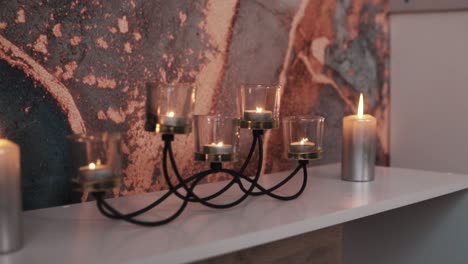 close-up-of-beautiful-burning-candles-on-a-dresser-against-a-backdrop-of-wallpaper-with-abstract-patterns