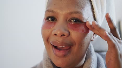 Happy-african-american-plus-size-woman-applying-under-eye-patches,-unaltered,-slow-motion