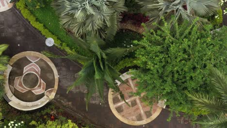 bird eye view of a small park inside a city, showing the walking path with benches put in designated circles and many tropical looking palm trees