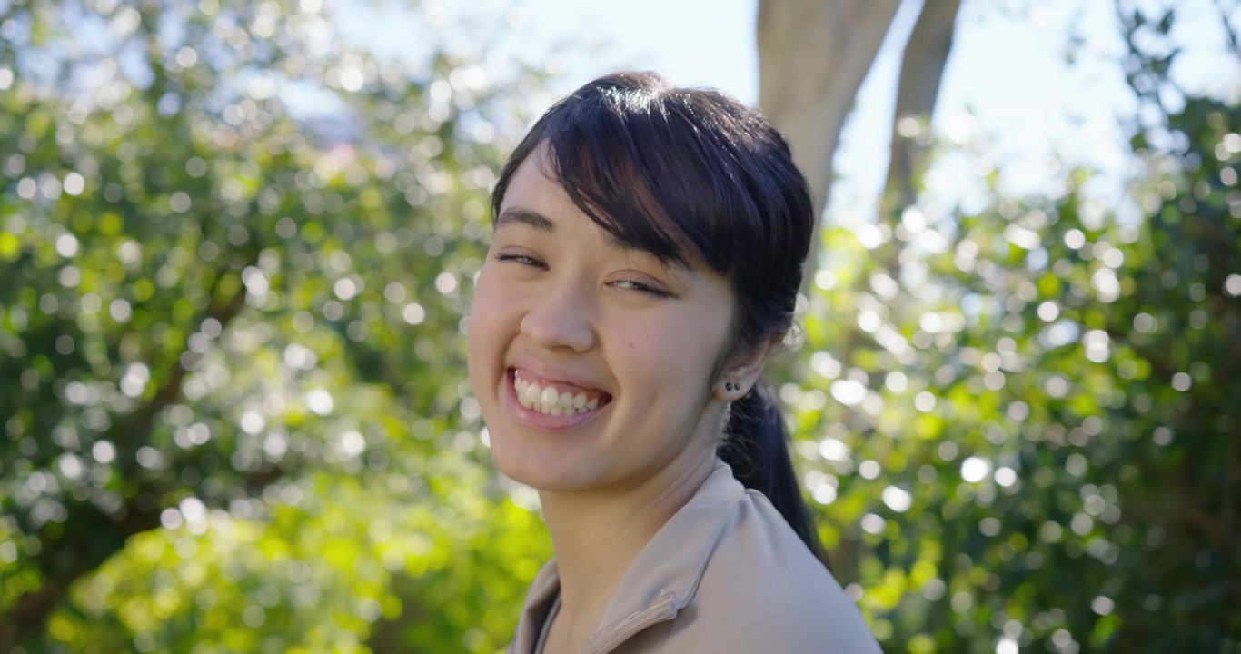 花园中，一位戴白色发带的非裔美国女性，低头后转向镜头，面带微笑走近。