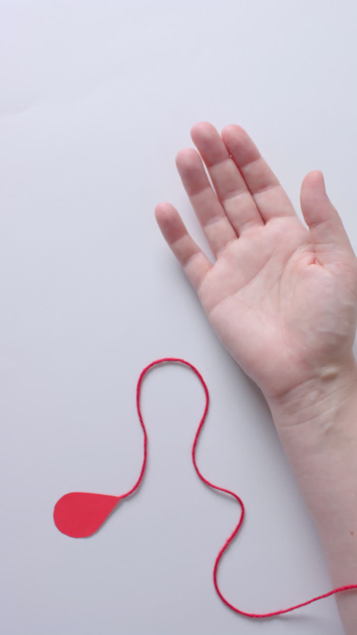 Vertical video of hand of caucasian man with blood drop, red string and heart, slow motion