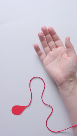vertical video of hand of caucasian man with blood drop, red string and heart, slow motion