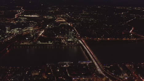 AERIAL:-Beautiful-Wide-Shot-over-Cologne-Germany-with-River-Rhine-and-Bridge-Car-traffic-and-City-lights