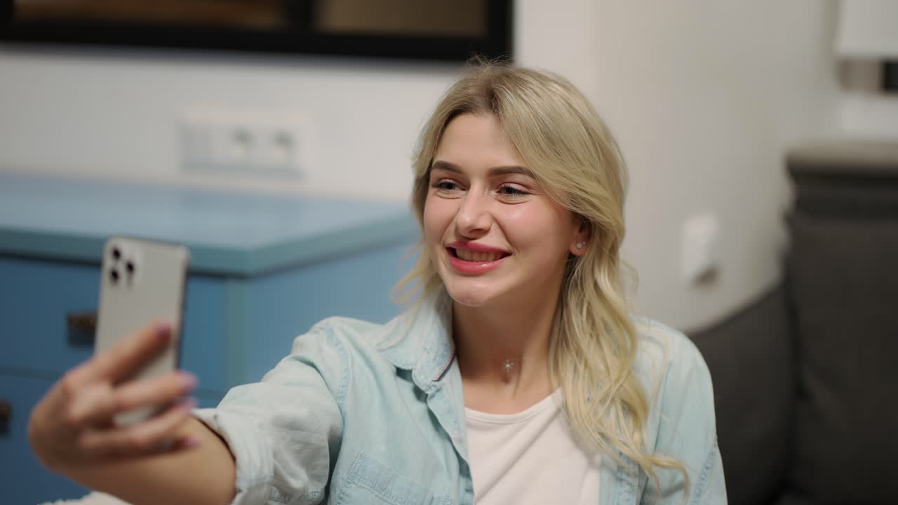 mujer rubia posando en la cámara del teléfono inteligente en casa