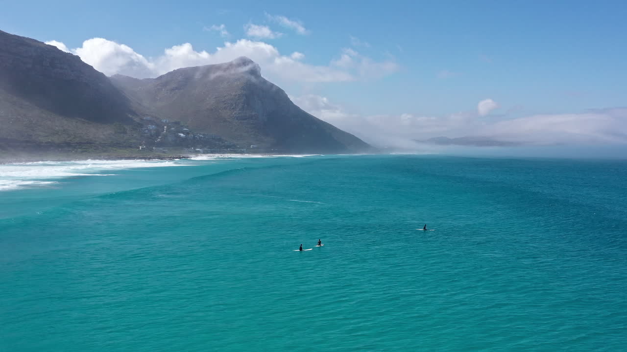 surfistas esperando olas en sudáfrica montañas en el fondo día soleado