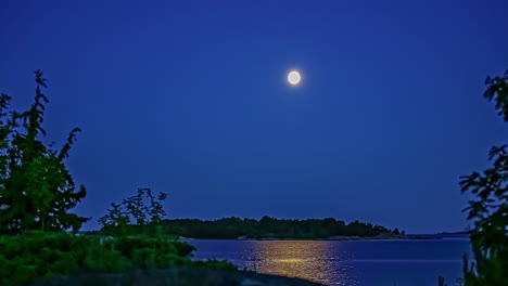 full moon crossing the sky over an island across a bay - nighttime time lapse